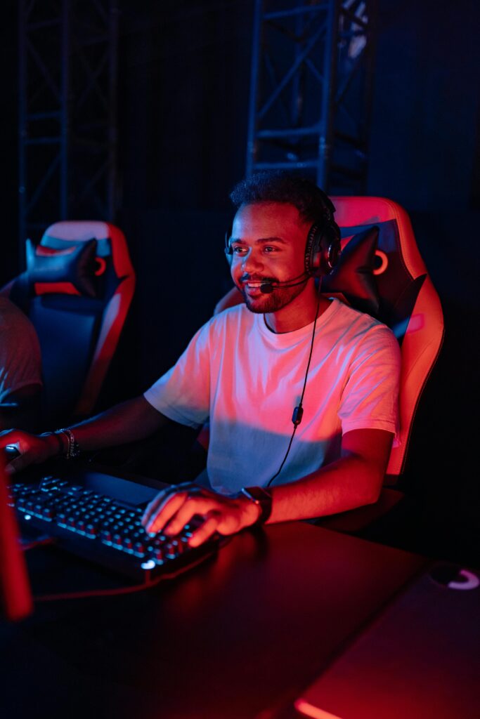 An African American man engaged in gaming at a computer station, wearing a headset.