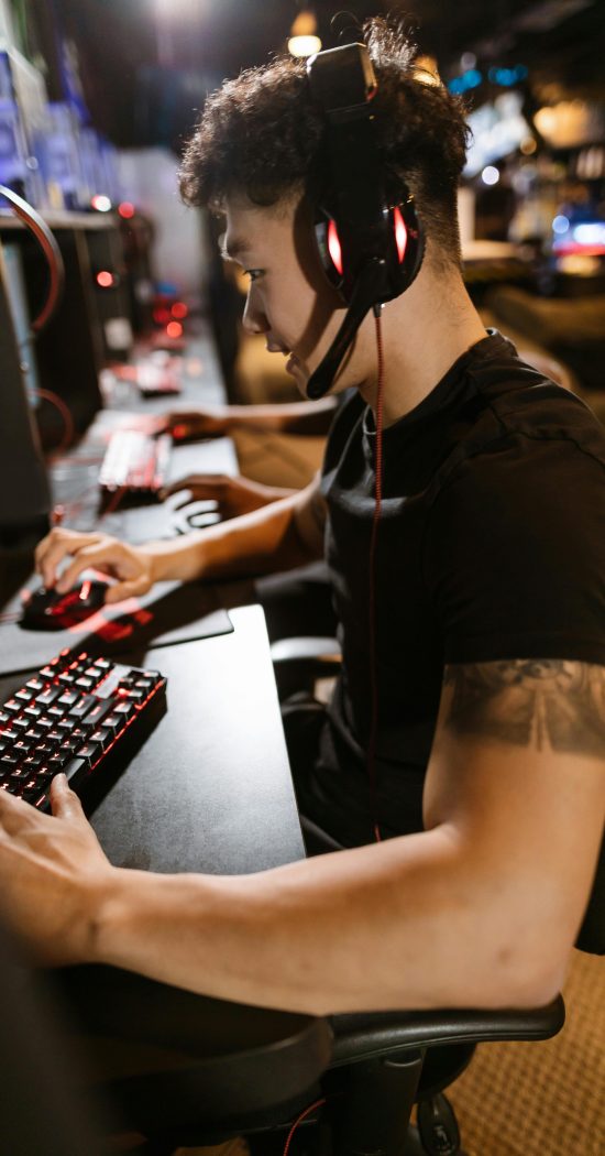 A gamer wearing headphones intensely focused on gaming in a cyber-themed arcade.