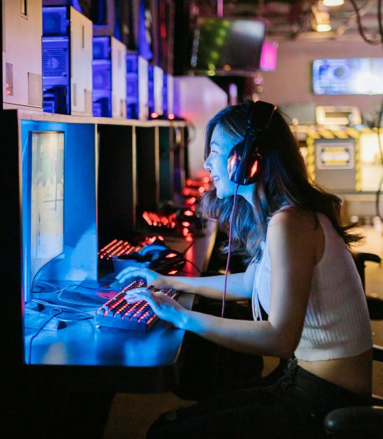 A woman intensely focused on a gaming computer in an esports setting with vibrant lighting.